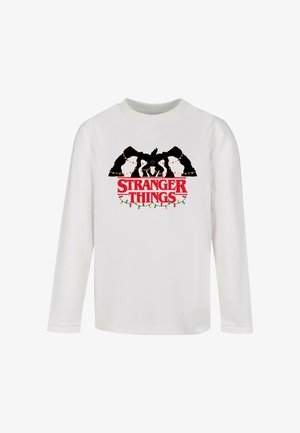 Balta ilgomis rankovėmis marškiniai su juodu grafiniu piešiniu, vaizduojančiu personažus su spalvingomis šventinėmis lemputėmis ir ryškiu raudonu užrašu "STRANGER THINGS".