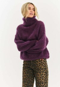 Fialový mohairový sveter s vysokým golierom, oversize strihom a rebrovanými manžetami v kombinácii s hnedými nohavicami s leopardím vzorom. Mäkká textúra, voľný tvar.