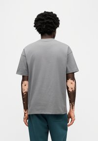 Γκρι κοντομάνικη μπλούζα με στρογγυλή λαιμόκοψη, κατασκευασμένη από μαλακό βαμβάκι, με χαλαρή εφαρμογή και λεία υφή, σε προβολή από πίσω.