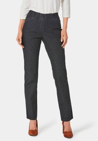 Jean foncé avec une taille élastique, coupe droite, et détails de couture subtils, assortis à des chaussures à talons hauts marron.