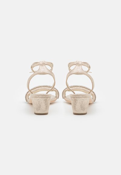 Beige glitterkengät korokkeella, joissa on nilkkahihna ja solmusesityö. Ominaisuuksina teksturoitu materiaali ja paksu korko. Avoin takasuunnittelu.