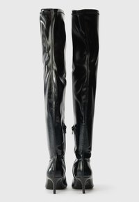 Sorte over kneet støvler laget av blank lær, med stiletthæl og glidelåser på siden for feste. Glatt tekstur og slank profil.