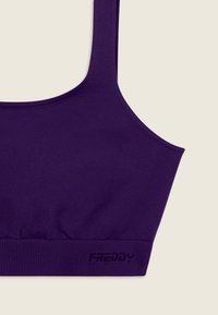 Sujetador deportivo morado con tirantes anchos y banda inferior acanalada, colocado plano sobre un fondo claro.