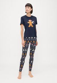 Camiseta de algodón azul marino con un gráfico de un hombre de jengibre; combinada con leggings elásticos que muestran patrones temáticos de vacaciones en varios colores.