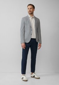 Szary, teksturowany żakiet na lekki polo, granatowe slim-fit spodnie i białe sneakersy z czarnymi akcentami. Czysty design, dopasowany krój.
