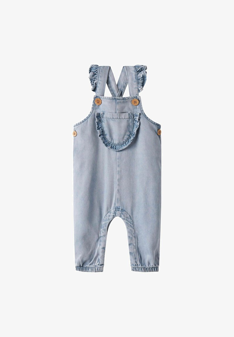 Peto de mezclilla azul claro con tirantes con volantes, dos botones de madera y un bolsillo redondo con borde con volantes en la parte frontal.