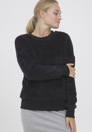 Sweatshirt en molleton noir, doux au toucher, avec un col rond et des poignets en ribbed noirs. Présente une texture douce et une coupe décontractée.