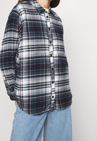 Flannel shirt featuring a plaid pattern in navy, white, green, and pink, with a button-down front and a collar. Soft texture.
