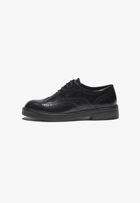 Svart läder brogue-sko med dekorativa perforeringar och krökta designelement. Har en robust sula och traditionell snörning.