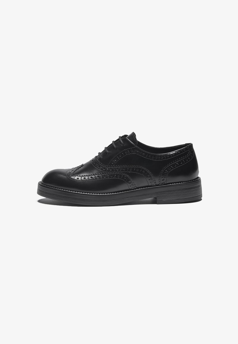 Svart läder brogue-sko med dekorativa perforeringar och krökta designelement. Har en robust sula och traditionell snörning.