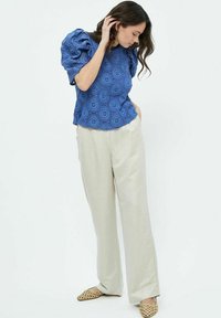 Top blu textured con maniche a palloncino, con motivi circolari, abbinato a pantaloni a gamba larga beige chiaro e scarpe slip-on beige con motivo.