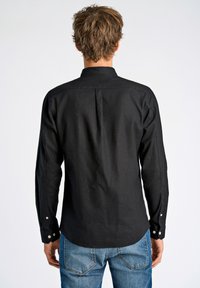 Zwarte lange mouw shirt met een bandkraag. Bevat knoopsluitingen op de mouwen, textuurstof en een rugpas voor extra detail.
