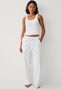 Witte pyjamabroek met blauwe hartpatronen, met een geribbelde textuur, wijde pijpen en een elastische tailleband. Gecombineerd met een witte tanktop.