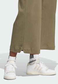 Vita sneakers med beige accenter och tre ränder. Klickas med ribbade olivgröna byxor som har en liten spricka vid fållen.