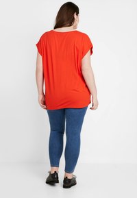 Rød oversized t-skjorte med korte ermer, glatt tekstur, droppede skuldre, kombinert med blå smale jeans og svarte snøresko.