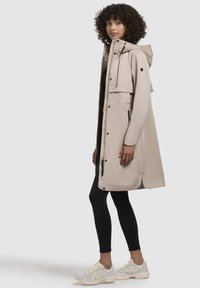 Beige vízálló parka kapucnival, elülső zsebekkel és cipzárral. Sima, könnyű anyag, laza szabással, fekete leggings-szel és sportcipőkkel párosítva.