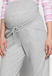 Grå graviditetssvetter med elastisk linning, justerbar snor og myk tekstur; tettsittende design som gir plass til en voksende mage.