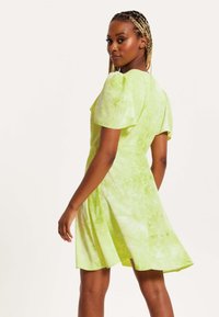 Short, green tie-dye dress with puff sleeves, fitted bodice, and flared skirt. Lightweight fabric with a soft, smooth texture.