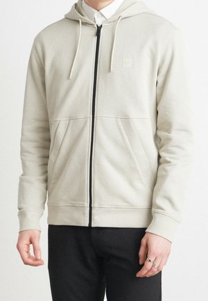 Light gray zip-up hoodie with a black zipper, kangaroo pockets, and drawstring hood. Smooth fabric with ribbed cuffs. Subtle logo detail.