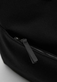Sac en tissu noir avec une poche zippée dotée d'une tirette en cuir texturé, surface en textile lisse et design minimaliste.