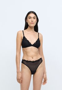 Ensemble de lingerie noire comprenant un bralette en forme triangulaire avec des bordures en dentelle et une culotte assortie en tulle avec des bords en vagues.