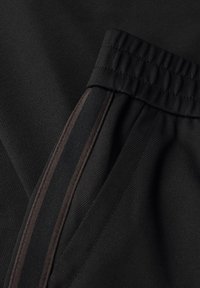 Tessuto nero con una finitura testurizzata, caratterizzato da un orlo cucito e una cerniera laterale con un accento marrone scuro lungo la cucitura.