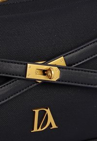 Bolsa de tela negra con textura, que presenta herrajes dorados, un mecanismo de cierre distintivo y un logo grabado en la esquina inferior.