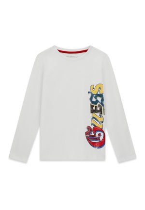 Chemise blanche à manches longues avec un grand texte vertical coloré "GUESS" sur le côté droit en lettres rouges, jaunes, bleues et noires.