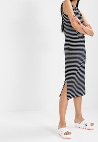 Abito senza maniche a righe in bianco e nero, lunghezza al ginocchio con spacco laterale, abbinato a sandali platform bianchi con suole rosa.