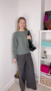Pull côtelé vert clair avec encolure bateau ; associé à un pantalon large gris foncé à jambe évasée. Sac à main noir et accessoires blancs visibles.