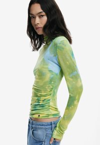 Top a maniche lunghe in tie-dye verde e blu con una vestibilità aderente. Presenta un tessuto morbido e testurizzato e dettagli arricciati lungo i lati.