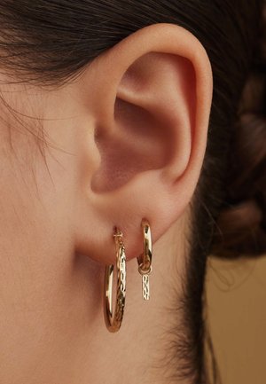 Gouden creolen tentoongesteld aan een oor, met een grote, gestructureerde ring en een kleinere, gladde ring met een hangend accentstuk.