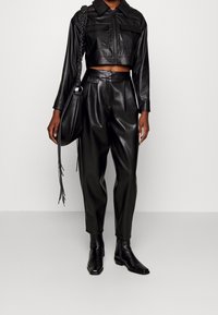 Zwarte leren cropped jack met rits aan de voorkant en twee zakken, gecombineerd met zwarte leren broek. Details zijn onder meer een tas met kettingriem en strakke laarzen.