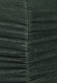 Temno zelena tkanina z teksturiranim, nabranim vzorcem, ki ima svilnat sijaj in gladek zaključek. Šivi so vidni ob robovih.