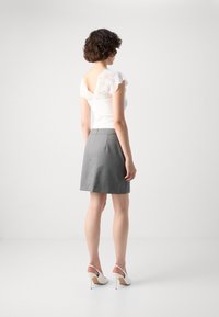 Hvit topp med blonde ermer, grå skjørt og hvite slingback-hæler. Toppens design har V-rygg, mens skjørtet har en tettsittende silhuett.