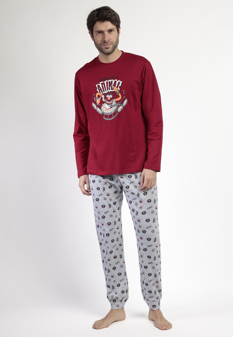 Hombre con una camiseta de manga larga roja con un batería de dibujos animados y pantalones de pijama grises con pequeñas caras de dibujos animados similares y patrones.