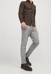 Brun långärmad skjorta med knappar i kombination med grå rutiga slim-fit byxor och svarta loafers, med en strukturerad design och rena linjer.