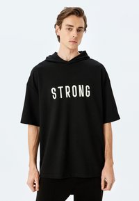 Sudadera con capucha negra que presenta un bold texto blanco "STRONG" en la parte frontal, hecha de un material suave, con mangas cortas y un corte relajado.