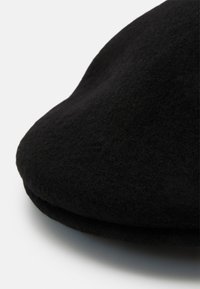 Cască din lână neagră cu o formă rotundă și o textură moale, având un bor întors. Materialul pare neted și dens, potrivit pentru vreme rece.