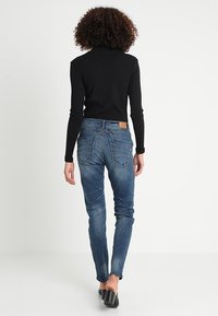 Czarny prążkowany top z długim rękawem zestawiony z niebieskimi slim-fit jeansami o teksturowanym wykończeniu i tylnymi kieszeniami. Modelka nosi czarne szpilki.