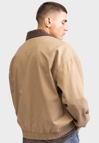 Brown bomber jacket with a corduroy collar, elasticized waistband, and long sleeves. Smooth fabric with a relaxed, classic fit.