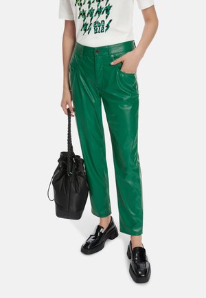 Grüne, glänzende Kunstlederhosen mit einer hochtaillierten Passform, seitlichen Taschen und geradem Bein. Kombiniert mit einer schwarzen Tasche und Schuhen.