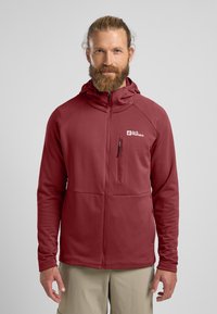 Rode fleecejas met een ritssluiting aan de voorkant, een capuchon en een gestructureerde stof. Bevat een logo op de borst en een ritszak aan de linkerkant.