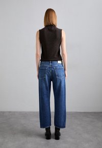 Svart ärmlös topp, blå vida denimjeans, hög midja med bakfickor, bärs med svarta ankelboots. Minimalistisk design, avslappnad passform.