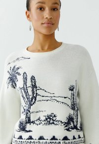 Witte gebreide trui met een marineblauw woestijnlandschapontwerp met cactussen en palmbomen. Ronde halslijn en verlaagde schouders. Getextureerde stof.