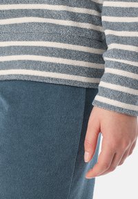 Pruhovaná tkanina v námořnické modři a bílé barvě, texturovaná a měkká. Ruka spočívá na hladkém, tmavě modrém oděvu vyrobeném z materiálu podobného froté.