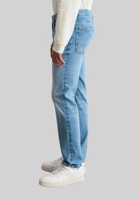 Jean en denim bleu clair avec une coupe droite. Comprend deux poches arrière et des coutures discrètes. Associé à des baskets blanches.