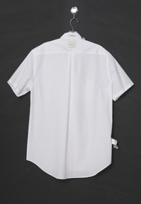 White short-sleeve shirt with a collar hanging on a metal hanger against a dark background, viewed from the back.