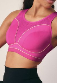 Fuchsia sport-bh met een gestructureerd mesh-paneel, gouden accenten en een ondersteunend ontwerp. Beschikt over een brede band en een slanke, contourniveau vorm.