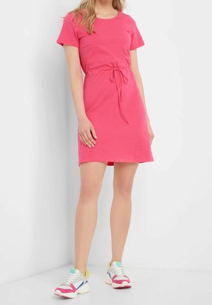 Vaaleanpunainen lyhythihainen mekko, jossa on kiristysnyörit vyötäröllä, valmistettu pehmeästä kankaasta. Yhdistetty monivärisiin tennareihin. Yksinkertainen polvenpituinen malli.